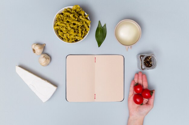 Tomates cerises rouges avec ingrédient pour pâtes et cahier ouvert