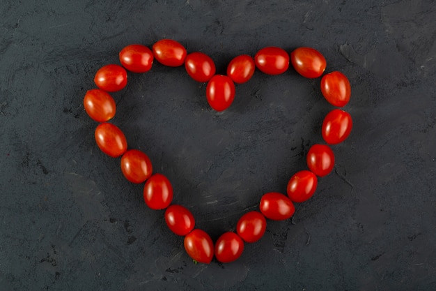 Tomates cerises tomates cerises rouges en forme de coeur sur un bureau sombre