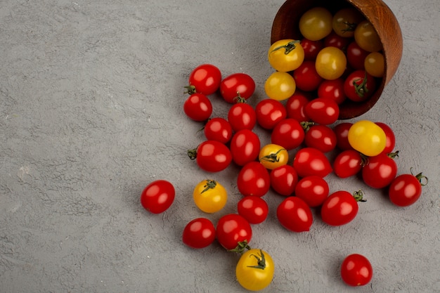Tomates colorées rouges et jaunes fraîches mûres à l'intérieur et à l'extérieur du pot rond marron sur le bureau gris
