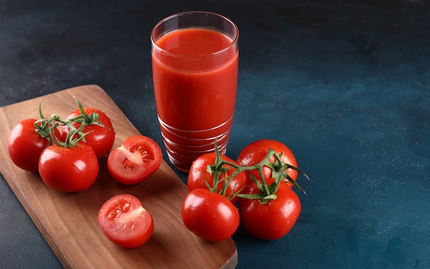 Photo gratuite tomates entières et coupées et un verre de jus de tomate sur le fond bleu.