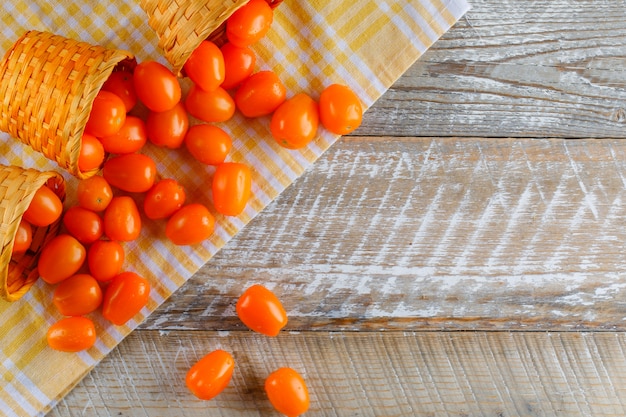 Tomates éparpillées de paniers en osier à plat poser sur un tissu de pique-nique et une table en bois