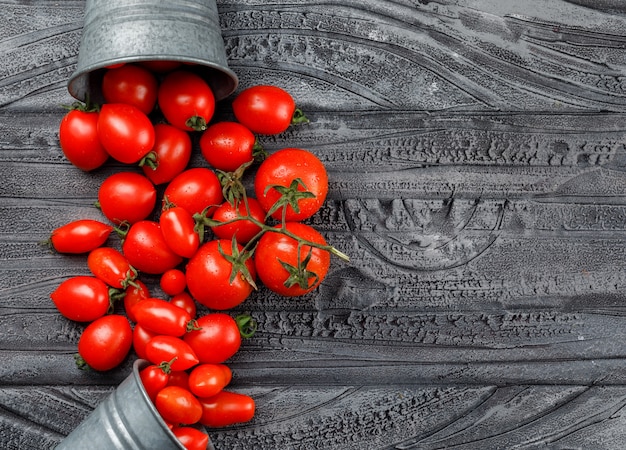 Photo gratuite tomates éparses de mini seaux sur un mur en bois gris. vue de dessus.