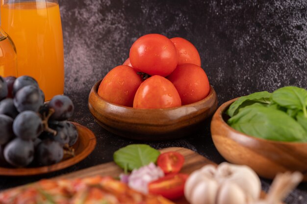 Tomates fraîches dans une tasse en bois, raisins et jus d'orange dans un verre.