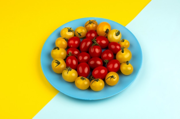 Tomates fraîches mûres rouges et jaunes à l'intérieur de la plaque bleue sur le bureau bleu glacier et jaune