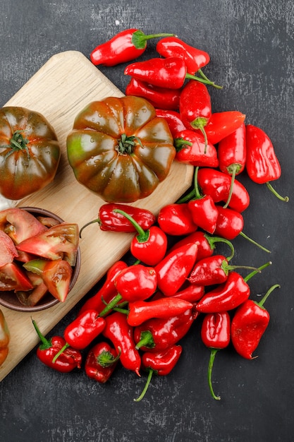 Tomates Kumato avec tranches, poivrons rouges vue de dessus sur le mur gris et planche à découper