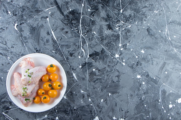 Tomates oranges et ailes de poulet sur une assiette , sur fond de marbre.
