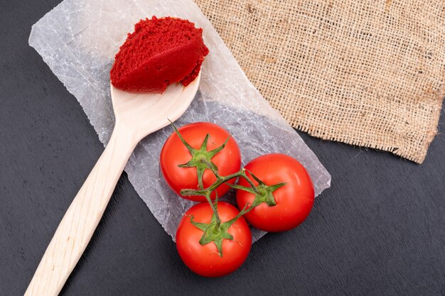 Tomates sur pâte de tomate en polyéthylène dans une cuillère en bois près du sac sur une surface en pierre noire