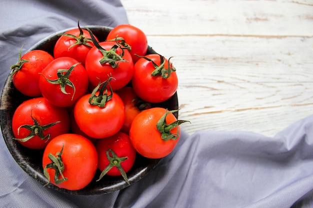 Tomates rouges biologiques fraîches dans une plaque noire sur une table en bois blanche avec des poivrons verts et rouges et rouges, des poivrons verts, des grains de poivre noirs, sel, gros plan, concept santé