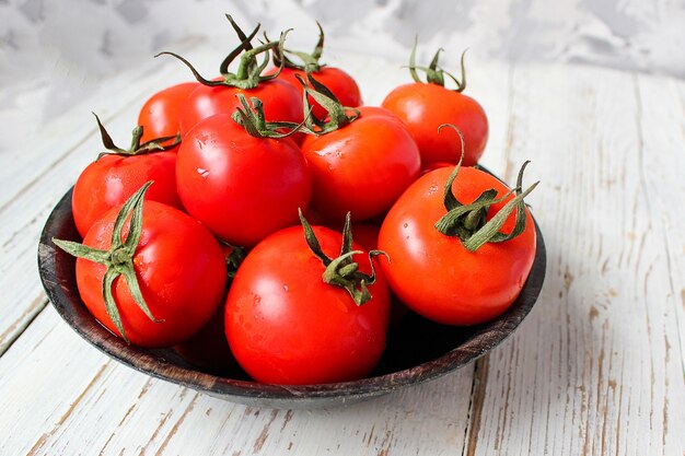 Tomates rouges biologiques fraîches dans une plaque noire sur une table en bois blanche avec des poivrons verts et rouges et rouges, des poivrons verts, des grains de poivre noirs, sel, gros plan, concept santé