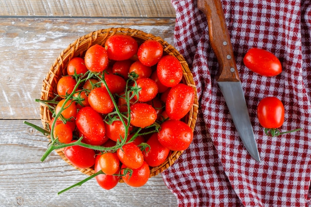 Photo gratuite tomates rouges dans un panier en osier avec un couteau à plat sur une serviette en bois et de cuisine