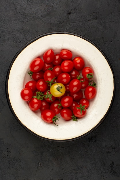 Photo gratuite tomates une vue de dessus de cerise rouge à l'intérieur de la plaque blanche sur fond sombre