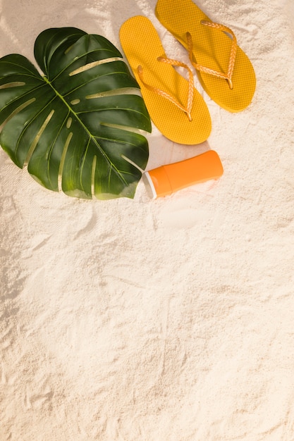 Photo gratuite tongs orange et feuilles de monstera sur la plage