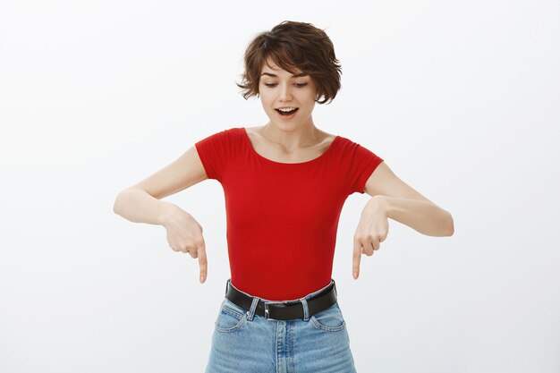 Étonné et excité jolie femme regardant vers le bas et pointant du doigt la bannière