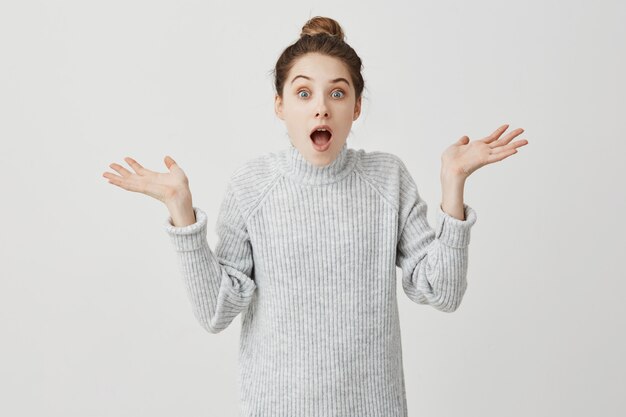 Étonné femme jetant des mains posant avec la bouche ouverte. Créateur de mode exprimant sa joie de montrer sur un mur blanc. Concept de joie