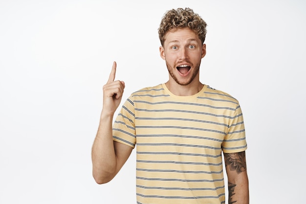 Étonné jeune homme blond pointant le doigt vers le haut mec crie d'excitation tout en montrant une annonce impressionnante recommandant un magasin avec fond blanc de vente