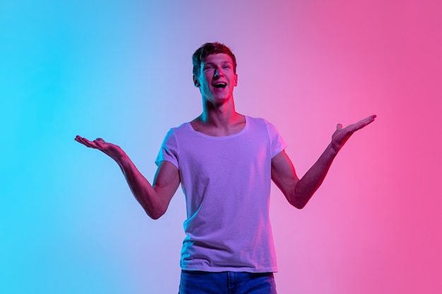 Étonné. Portrait de jeune homme caucasien sur fond de studio dégradé bleu-rose en néon. Concept de jeunesse, émotions humaines, expression faciale, ventes, publicité. Beau modèle en casual.