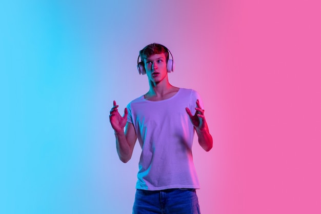 Étonné. Portrait de jeune homme caucasien sur fond de studio dégradé bleu-rose en néon. Concept de jeunesse, émotions humaines, expression faciale, ventes, publicité. Beau modèle en casual.