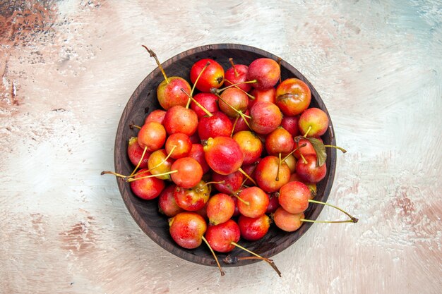 Top close-up view cerises bol de cerises rouge-jaune sur la table rose-blanc-gris