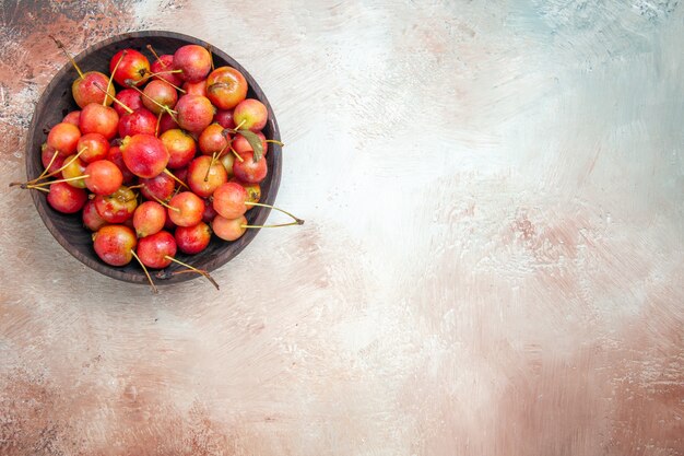 Top close-up view cerises bol de cerises sur la table rose-blanc-gris