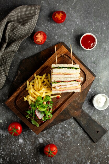 Top sandwich club avec des légumes frites et sauces sur large en bois