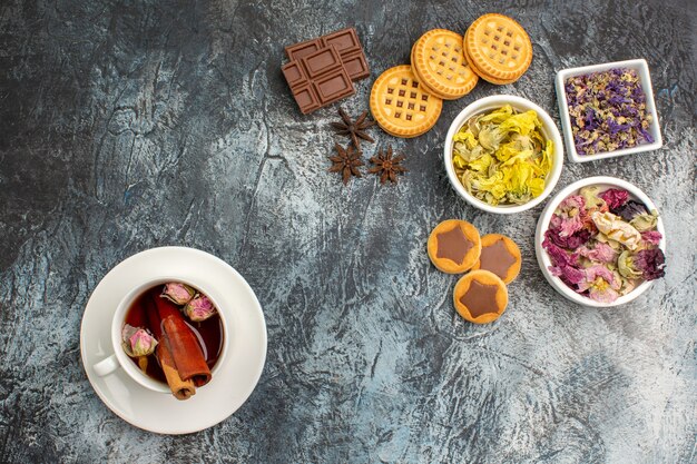 Top shot de tisane et bols de fleurs sèches et barres de chocolat avec des cookies sur fond gris