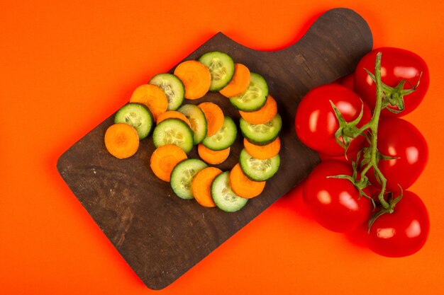 Top tranches de carotte et de concombre avec des tomates sur une planche à découper en bois sur orange