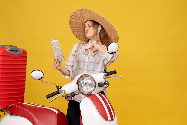 Top vie de fier jeune femme portant un chapeau ramassant ses bagages assis sur une moto et tenant une carte