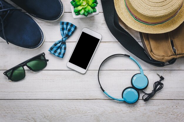 Top view accessoires pour voyager avec le concept d&#39;habillement homme. téléphone portable et casque sur fond en bois. Cravate, portefeuille, lunettes de soleil, chaussure, sac et chapeau sur table en bois.