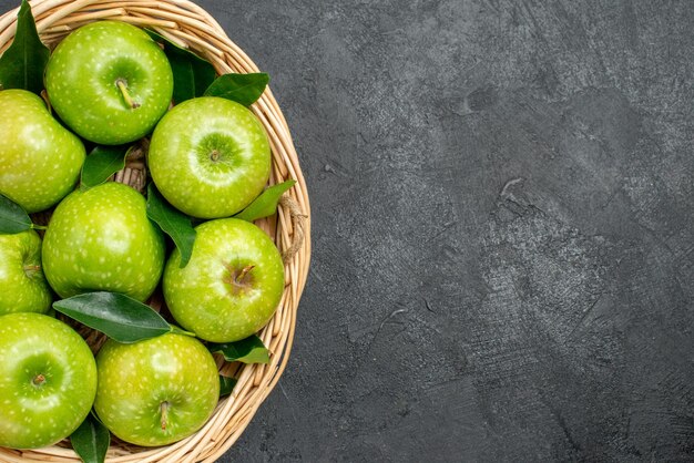 Top vue en gros plan des pommes dans le panier panier en bois des pommes appétissantes avec des feuilles vertes