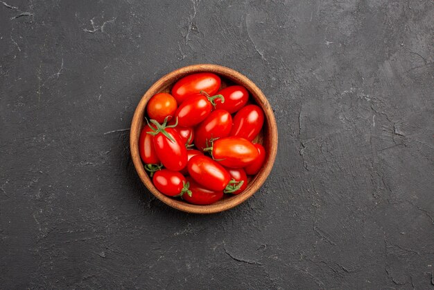 Top vue en gros plan tomates dans un bol tomates rouges mûres dans un bol au centre de la table sombre