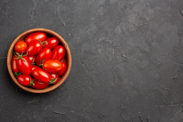 Top vue en gros plan tomates dans un bol tomates rouges mûres dans un bol sur le côté gauche de la table sombre