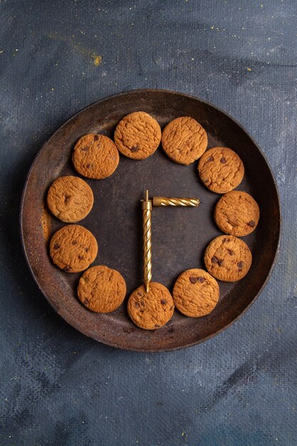 Top vue lointaine délicieux biscuits au chocolat à l'intérieur de la plaque ronde sombre sur le bureau gris foncé biscuit biscuit sweet