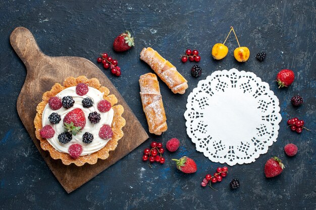 Top vue lointaine délicieux petit gâteau à la crème et aux baies avec des bracelets sur un bureau sombre, biscuit aux petits fruits