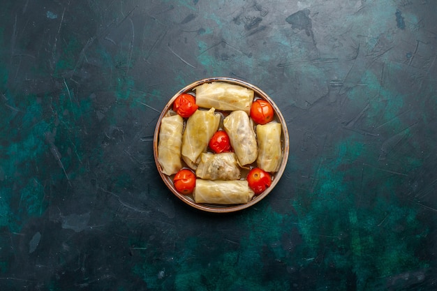 Top vue lointaine délicieux repas de viande roulé à l'intérieur de chou avec des tomates sur un bureau bleu foncé