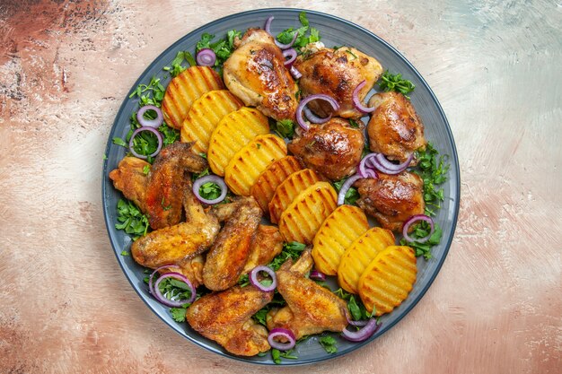 Top vue rapprochée ailes de poulet ailes de poulet tranches de pommes de terre frites herbes oignon sur la table