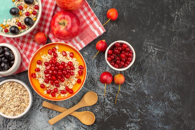 Top vue rapprochée baies bols de groseilles rouges cerises raisins pommes grenade cuillères d'avoine