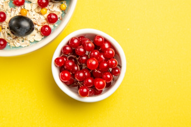 Top vue rapprochée des bols de baies des groseilles rouges appétissantes sur le tableau jaune