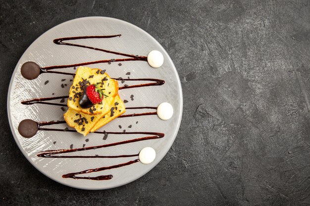 Top vue rapprochée dessert gâteau appétissant avec fraises et sauce au chocolat sur la plaque sur le côté gauche de la table sombre