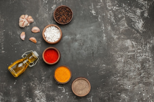 Top vue rapprochée épices cinq bols d'épices ail bouteille d'huile sur la table sombre