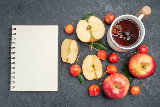 Top vue rapprochée fruits une tasse de thé pommes cerises avec des feuilles de cahier blanc