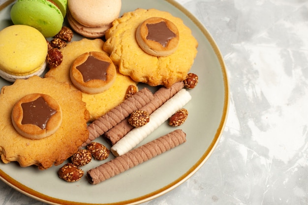 Top vue rapprochée macarons français avec des gâteaux et des biscuits sur une surface blanche légère