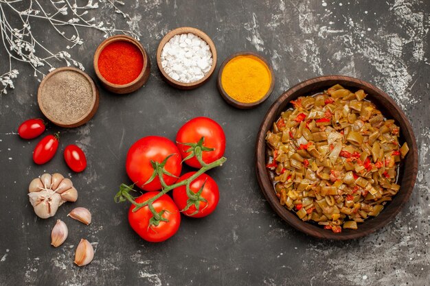 Top vue rapprochée plaque de haricots haricots verts tomates avec pédicelle à côté des bols d'épices colorées ail sur la table sombre