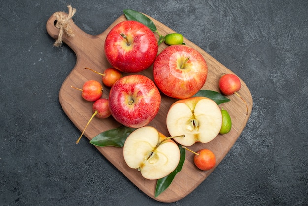 Top vue rapprochée pommes pommes cerises avec des feuilles sur la planche à découper