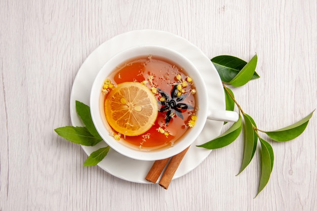 Top vue rapprochée tisane une tasse de tisane avec des bâtons de citron et de cannelle sur la soucoupe blanche et les feuilles de thé