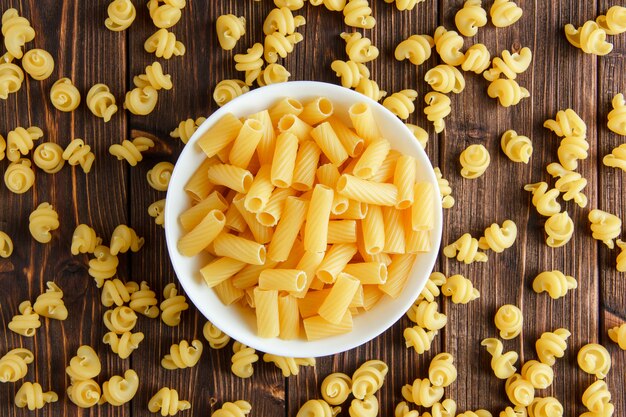 Tortiglioni dans un bol sur des pâtes en bois et crues. mise à plat.