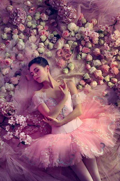 Touche de coucher de soleil. Vue de dessus de la belle jeune femme en tutu de ballet rose entouré de fleurs. Humeur printanière et tendresse à la lumière du corail. Concept de printemps, de fleurs et d'éveil de la nature.