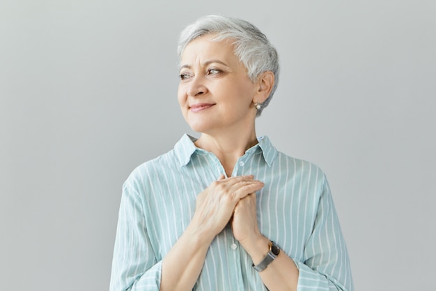 Photo gratuite touché reconnaissant charmant, retraité d'âge moyen, femme de race blanche à la recherche de suite avec un sourire reconnaissant, montrant sa gratitude et son appréciation pour l'amour, le soutien, les souhaits cordiaux, le soutien et les soins