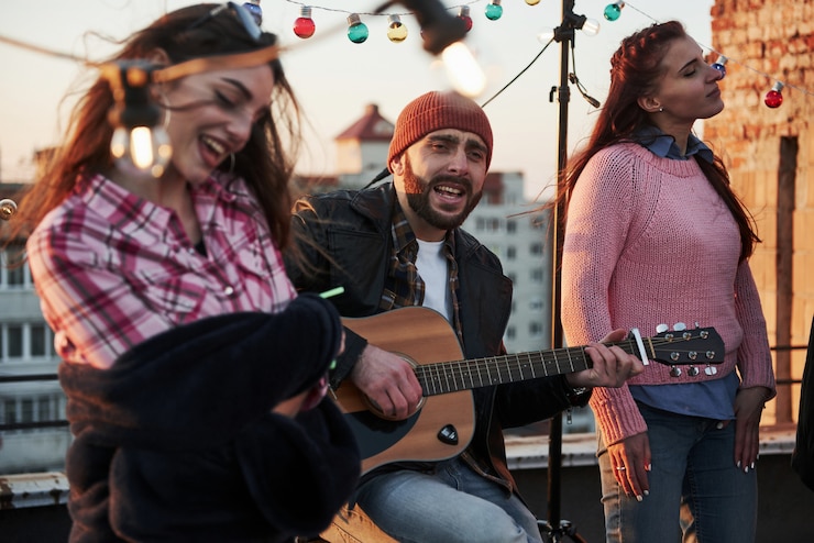 Photo gratuit toucher l'âme. trois amis s'amusent en chantant des chansons de guitare acoustique sur le toit