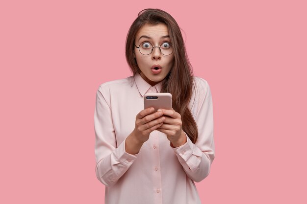 Tour de taille d'une femme caucasienne choquée tient un téléphone mobile, surpris de lire du spam, fait une erreur en tapant un message, reçoit des factures de téléphone élevées