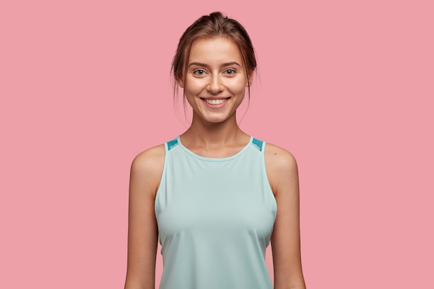 Tour de taille d'une femme caucasienne joyeuse avec une apparence attrayante, vêtue d'un gilet décontracté, satisfaite de l'entraînement sportif, modèle contre le mur rose. Concept d'expressions faciales et d'émotions